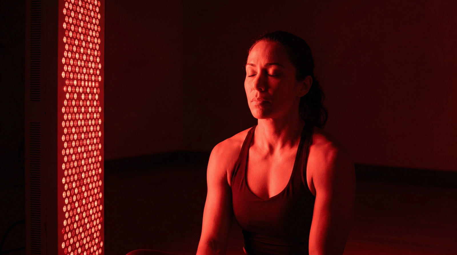 Athlete recovering in calm red light beside a Recon Restore red light therapy panel