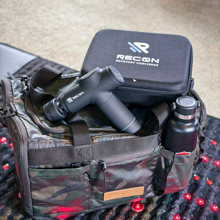 Recon recovery concierge equipment including a black bag, massage gun, and water bottle on a camouflage backpack.