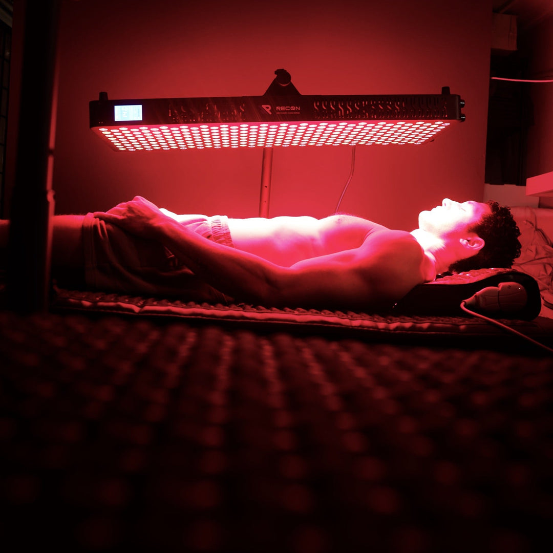 Person lying on a mat receiving red light therapy under a red light panel.