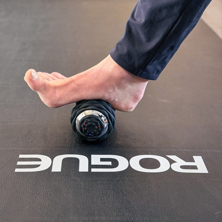 Person using a foam roller on a Rogue branded mat